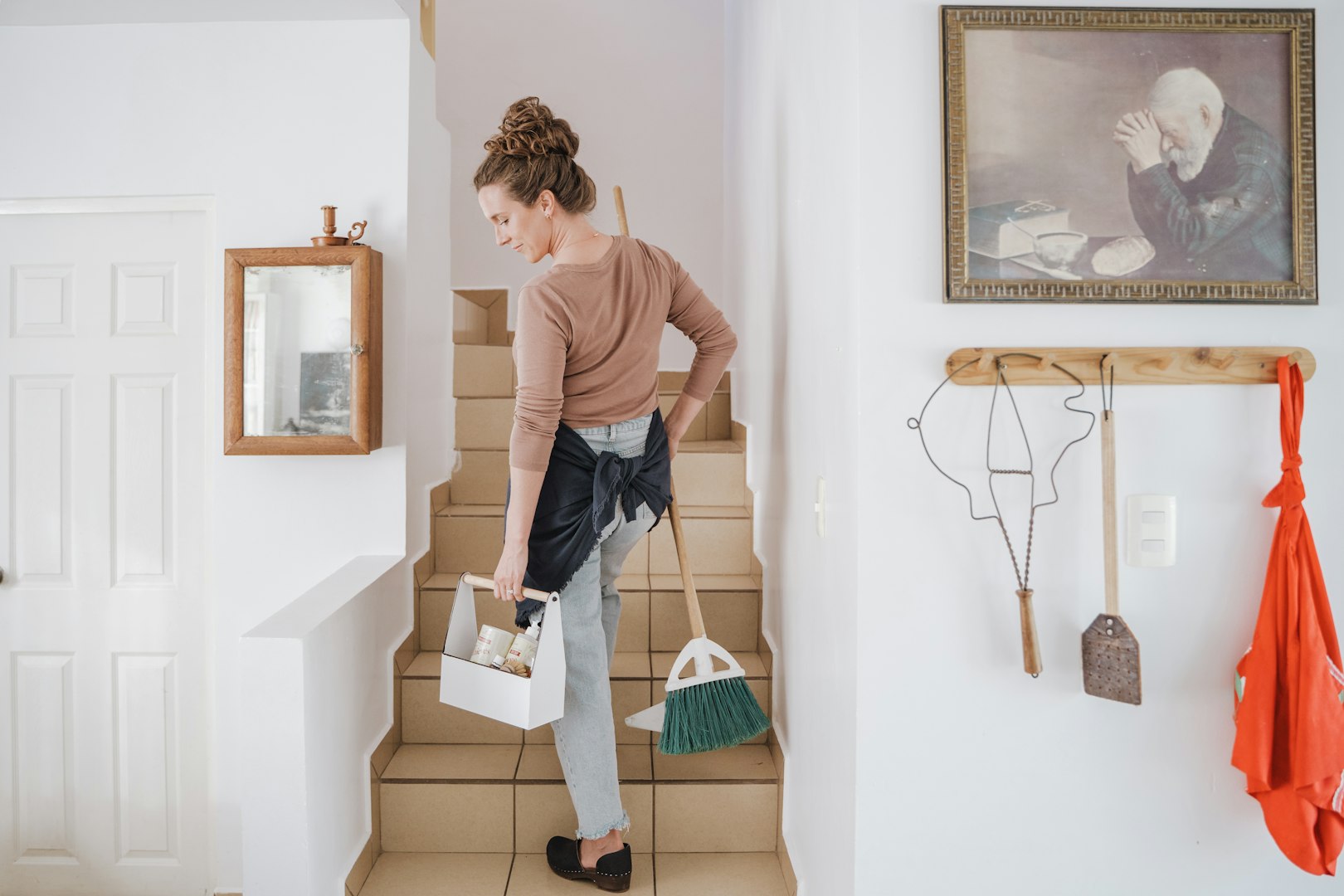 A woman vacuums a light carpet in a modern living room with a yellow sofa and a plant, wearing casual denim clothes and a headband.